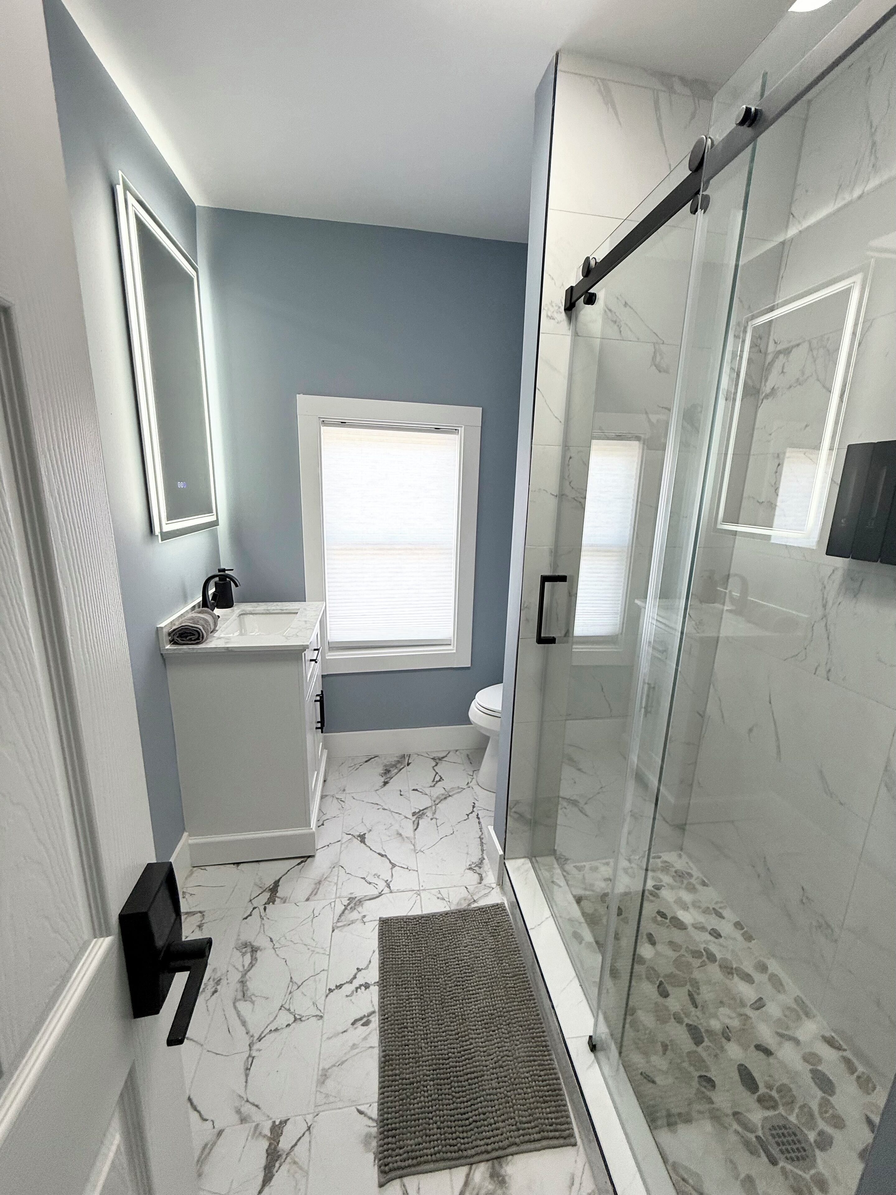 Un baño con cabina de ducha de vidrio, inodoro y lavamanos con espejo.