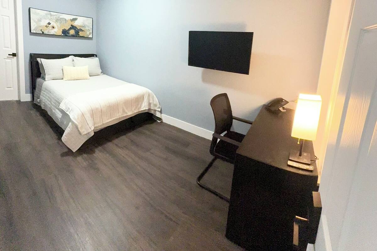 Ein Hotelzimmer mit einem Bett, einem Schreibtisch mit Lampe, einem Sessel und einem flachbildschirmfernseher an der Wand, sowie einer Tür.