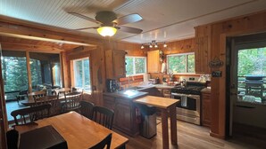 L’intérieur d’une cabane comprend un coin repas, une cuisine et de grandes fenêtres offrant une vue sur la forêt.