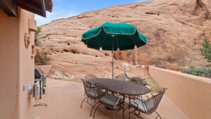 Eine Terrasse im Freien mit Tisch, Stühlen, einem grünen Sonnenschirm und einem Grill.