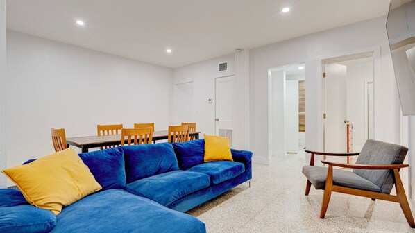 A modern living room with a blue sofa, wooden dining table, and chairs. - Marvelous 3-Bedroom Apartment in Miami (Miami)