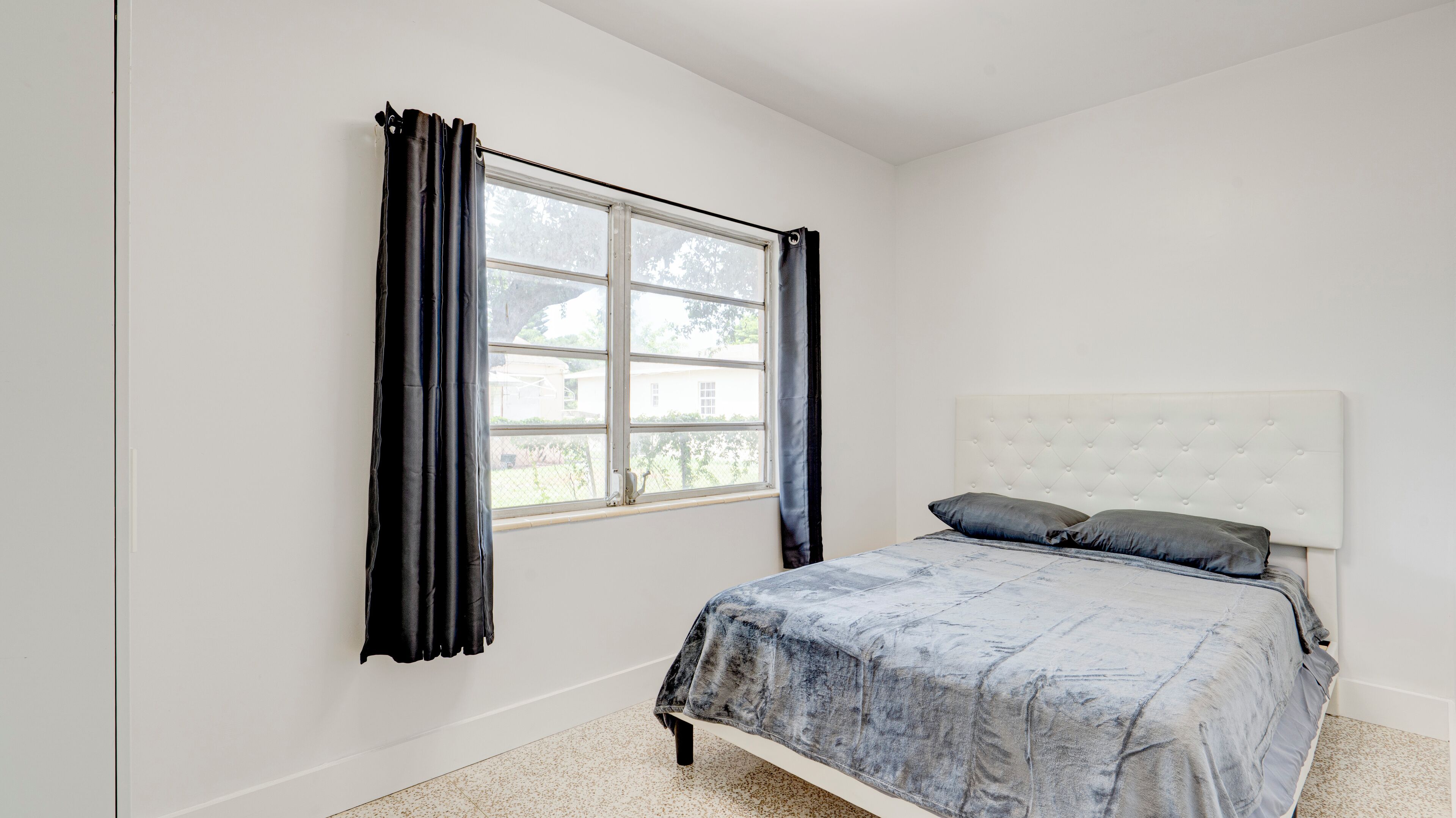 A bedroom with a bed, a window with curtains, and a view of the outside.