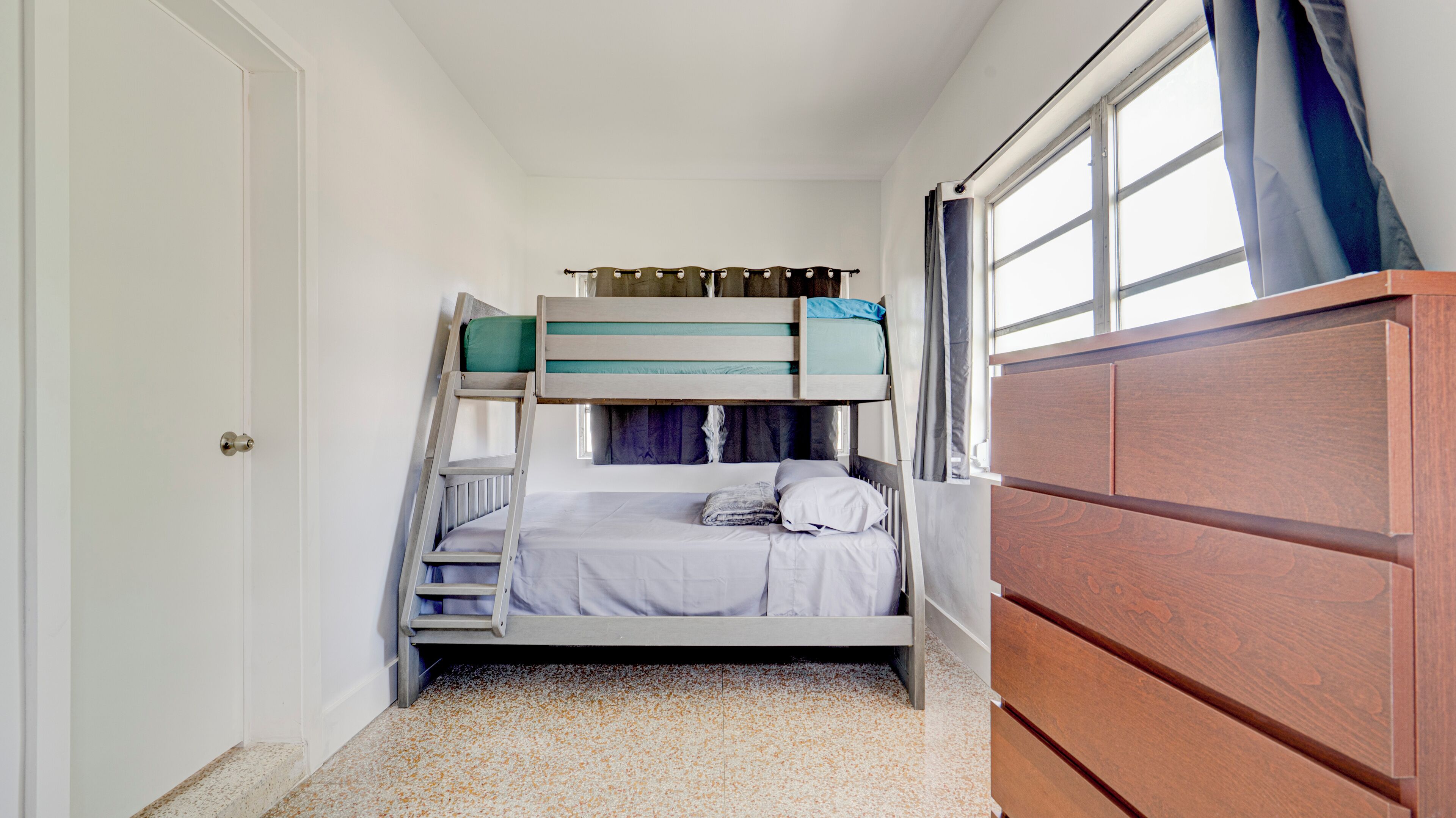 A compact room with a bunk bed, a wooden wardrobe, and a window with curtains.