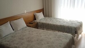 Une chambre d’hôtel avec deux lits, chacun doté d’une tête de lit en bois et d’une couvre-lit à motifs floraux. Il y a une table de chevet avec une lampe et une prise électrique au mur.