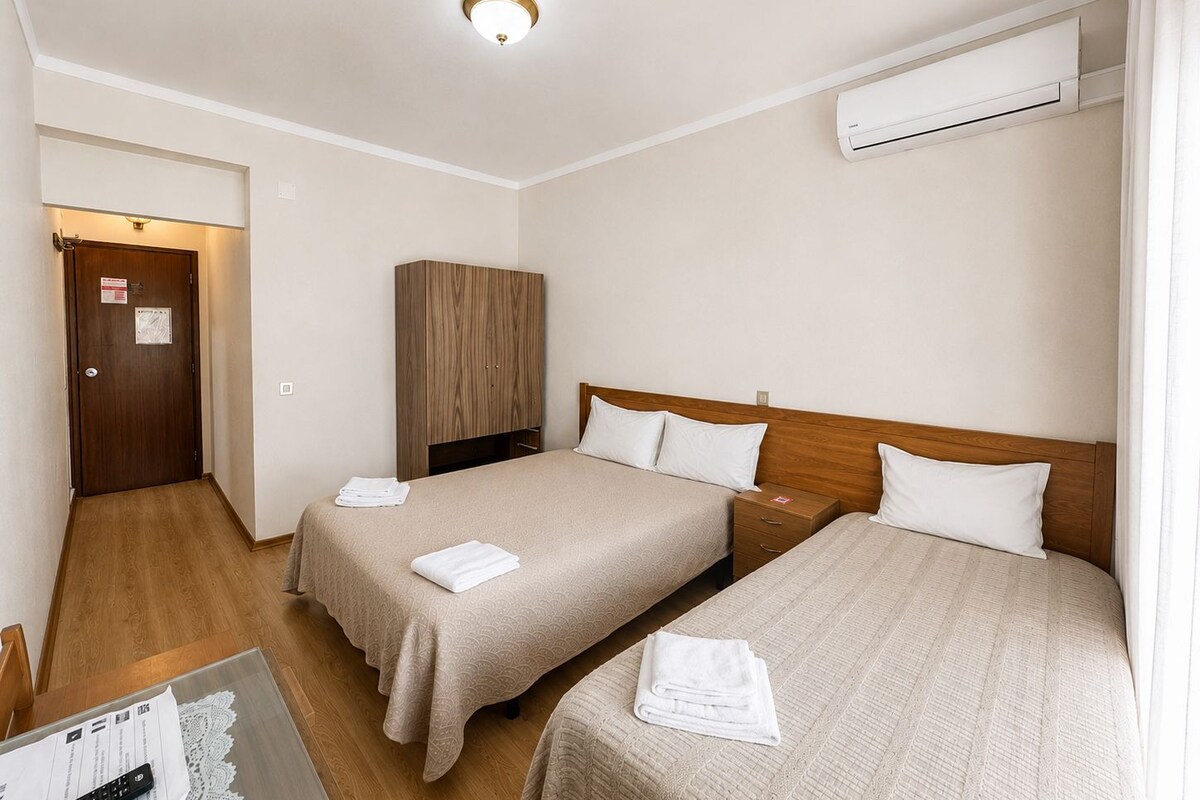 A hotel room with two beds, a wooden wardrobe, an air conditioning unit, and a door with a sign.