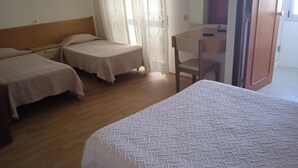 Une chambre d’hôtel avec deux lits simples, une tête de lit en bois, un petit bureau avec une chaise et une porte-fenêtre coulissante donnant sur un balcon.