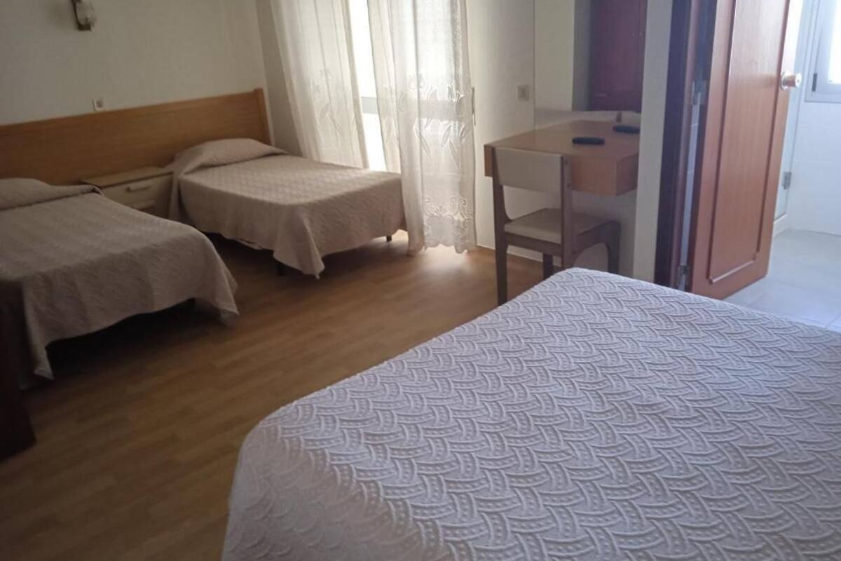 A hotel room with two single beds, a wooden headboard, a small desk with a chair, and a sliding glass door leading to a balcony.