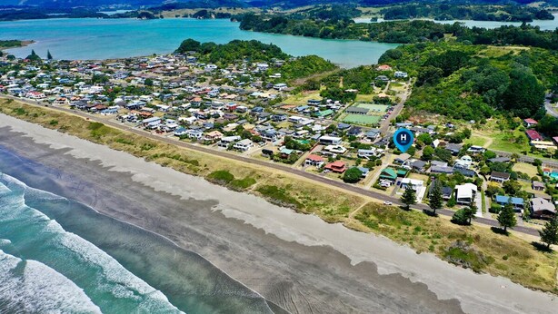Vista aérea de uma cidade costeira com praia, casas e um hospital.