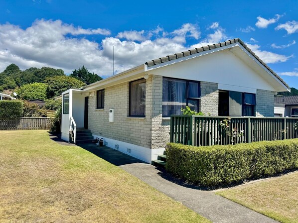 A single-story house with a sloped roof, a front porch, and a small front yard. - Ōhope Beach 3 Bedroom Holiday House (Ōhope)