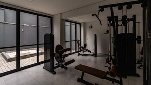 A gym with exercise equipment, large windows, and a bench.