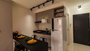 A compact kitchen with a black dining table, white cabinets, a stainless steel refrigerator, and a dark door.