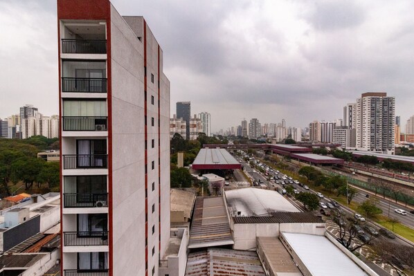 A high-rise building with multiple balconies, a cityscape in the background, and a busy road with vehicles.