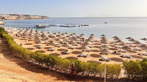 A beach with numerous sun loungers and umbrellas, a pier extending into the sea, and a clear view of the coastline. - Domina Coral Bay 1 or 2 rooms sea view terrace  (South Sinai Governorate)