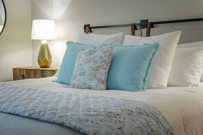 A bed with a quilted bedspread, multiple pillows, a bedside lamp, and a wooden nightstand. - Spacious Retreat Minutes from Samford (Birmingham)