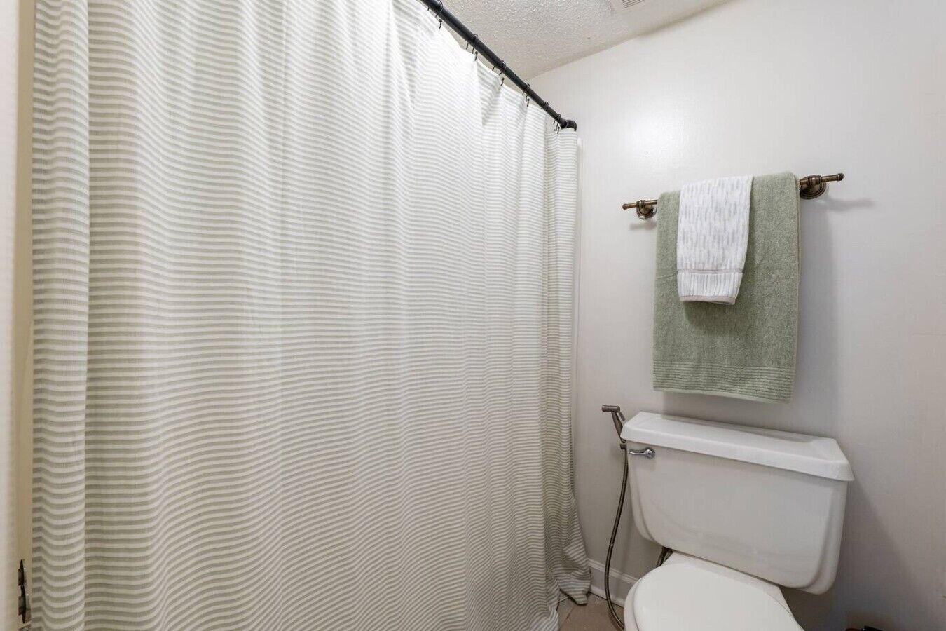 Un baño con cortina de ducha a rayas, un inodoro y un perchero con una toalla.