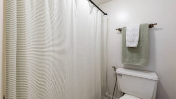 Un baño con cortina de ducha a rayas, un inodoro y un perchero con una toalla.