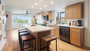 A modern kitchen with a large island, wooden cabinets, and a dishwasher. - Luxury 5BR Villa - Pool, Spa, Movie Theater, Game Room, Bar, & Outdoor Dining (La Mesa)