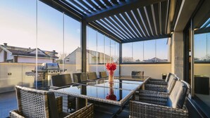 A modern outdoor dining area with a glass table and wicker chairs, overlooking a residential neighborhood. - Villa GIO’s ELITE: Design Villa with Pool and VIP Services near Monza Racetrack (Monza)