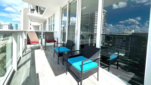 A balcony with wicker furniture and a glass railing, overlooking a cityscape. - Fully Remodeled 2 Bedroom with Direct Beach Access (Miami Beach)