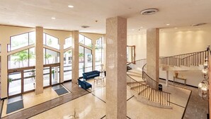 A spacious lobby with a blue sofa, a staircase, and large windows. - Fully Remodeled 2 Bedroom with Direct Beach Access (Miami Beach)