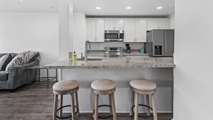 A modern kitchen with white cabinets, a stainless steel microwave, a refrigerator, and a granite countertop. There are three stools at the counter. - Modern 3-bed, 2-bath suite with a beautiful view of Topaz Lake. (Gardnerville)