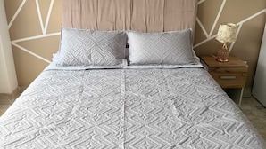 Una cama con una colcha de estampado geométrico y dos almohadas, una mesita de noche con una lámpara y una pared con diseño geométrico.
