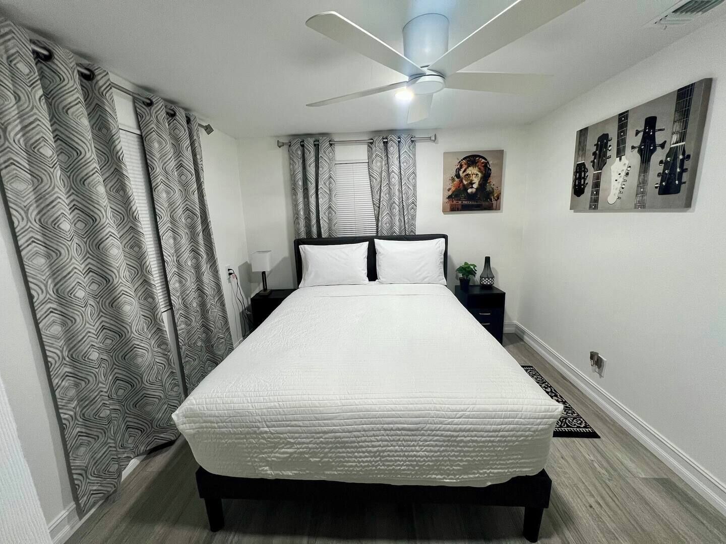 Una camera da letto ordinata con un letto, un comodino, una ventola a soffitto e una parete decorata con chitarre incorniciate.