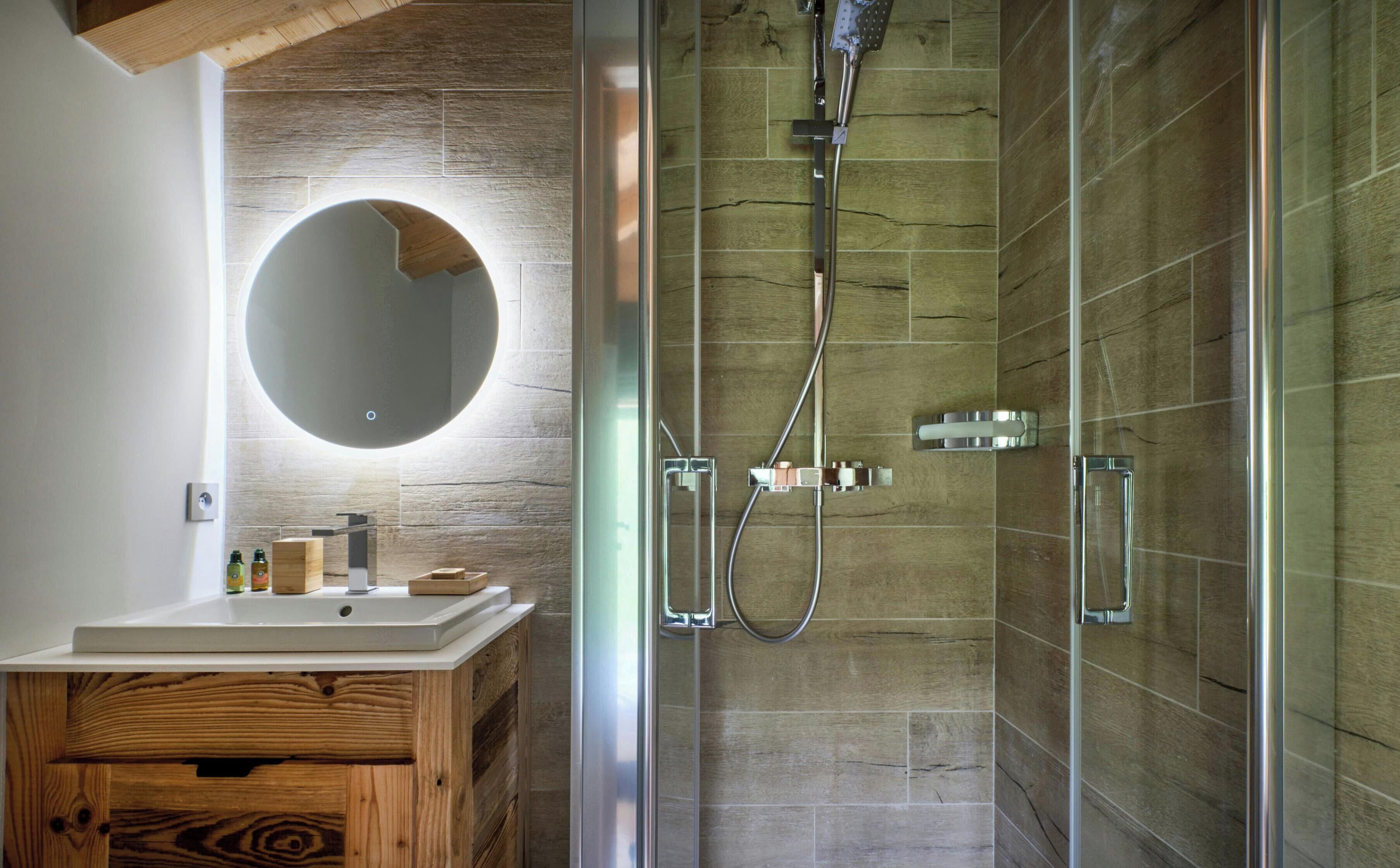 Ein modernes Badezimmer mit einem Holzbadezimmer-Möbelstück, einem runden Spiegel und einer Duschkabine mit einer Handbrause.