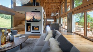 A modern interior with a fireplace, a television, and a large window overlooking a deck. - Chalet RevAlp - All-season holidays with private sauna - OVO Network (Combloux)