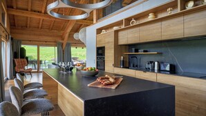 A modern kitchen with a large island, wooden cabinets, and a view of the outdoors. - Chalet RevAlp - All-season holidays with private sauna - OVO Network (Combloux)