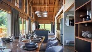 A modern dining area with a long table set for a meal, wooden beams on the ceiling, and a view of the outdoors. - Chalet RevAlp - All-season holidays with private sauna - OVO Network (Combloux)