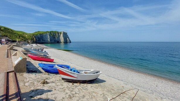 A beach with boats lined up on the shore, a rocky cliff in the background, and a clear sky.