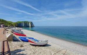 Une plage où des bateaux sont alignés le long du rivage, une falaise rocheuse en arrière-plan et un ciel dégagé.