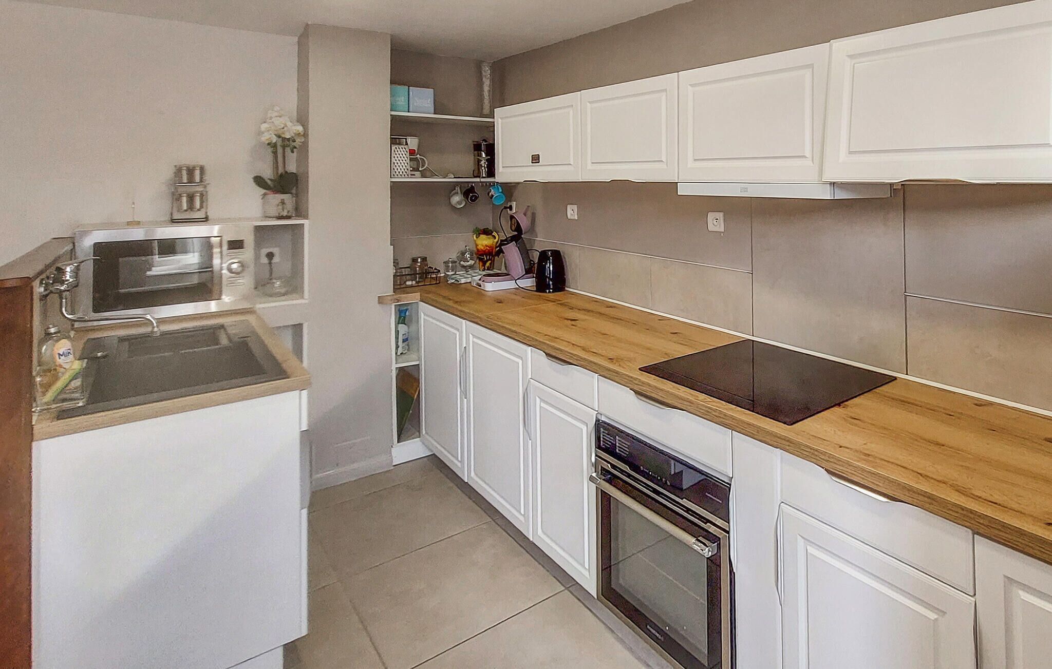 A compact kitchen with white cabinetry, a wooden countertop, a built-in oven, and a microwave.