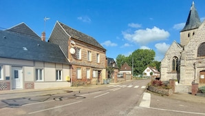 A street with buildings, including a church with a pointed steeple and a house with a sloped roof.