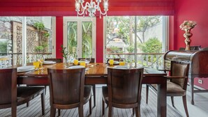 A dining area with a wooden table set for four, a chandelier, and a view of the outdoors. - XIX Writer’s Belle Époque Villa • Central Funchal • Tropical Garden • BBQ (Funchal)
