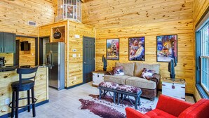 A cozy cabin interior with wooden walls, a kitchen area, a dining table, and a seating area with a sofa and ottomans.