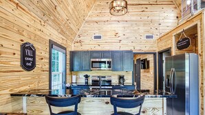 A modern kitchen with wooden walls, a central island with bar stools, stainless steel appliances, and a sign that reads "YALL come eat".