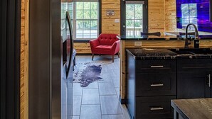 A spacious kitchen with a high ceiling, wooden walls, and a large window.