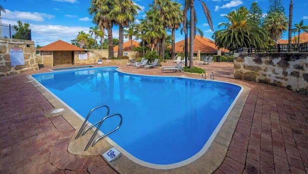 A swimming pool with a 1.9m depth marker, surrounded by palm trees and lounge chairs.