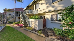 A two-story residential building with a balcony, a staircase, and a small garden area with plants and flowers.