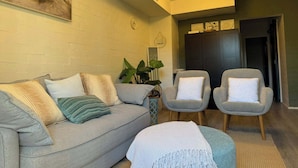 A living room with a grey sofa, two armchairs, a small table, and a plant.