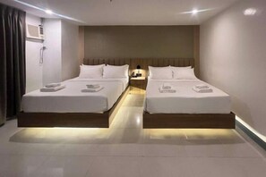 Habitación de hotel con dos camas, una mesita de noche con lámpara y un aire acondicionado instalado en la pared.