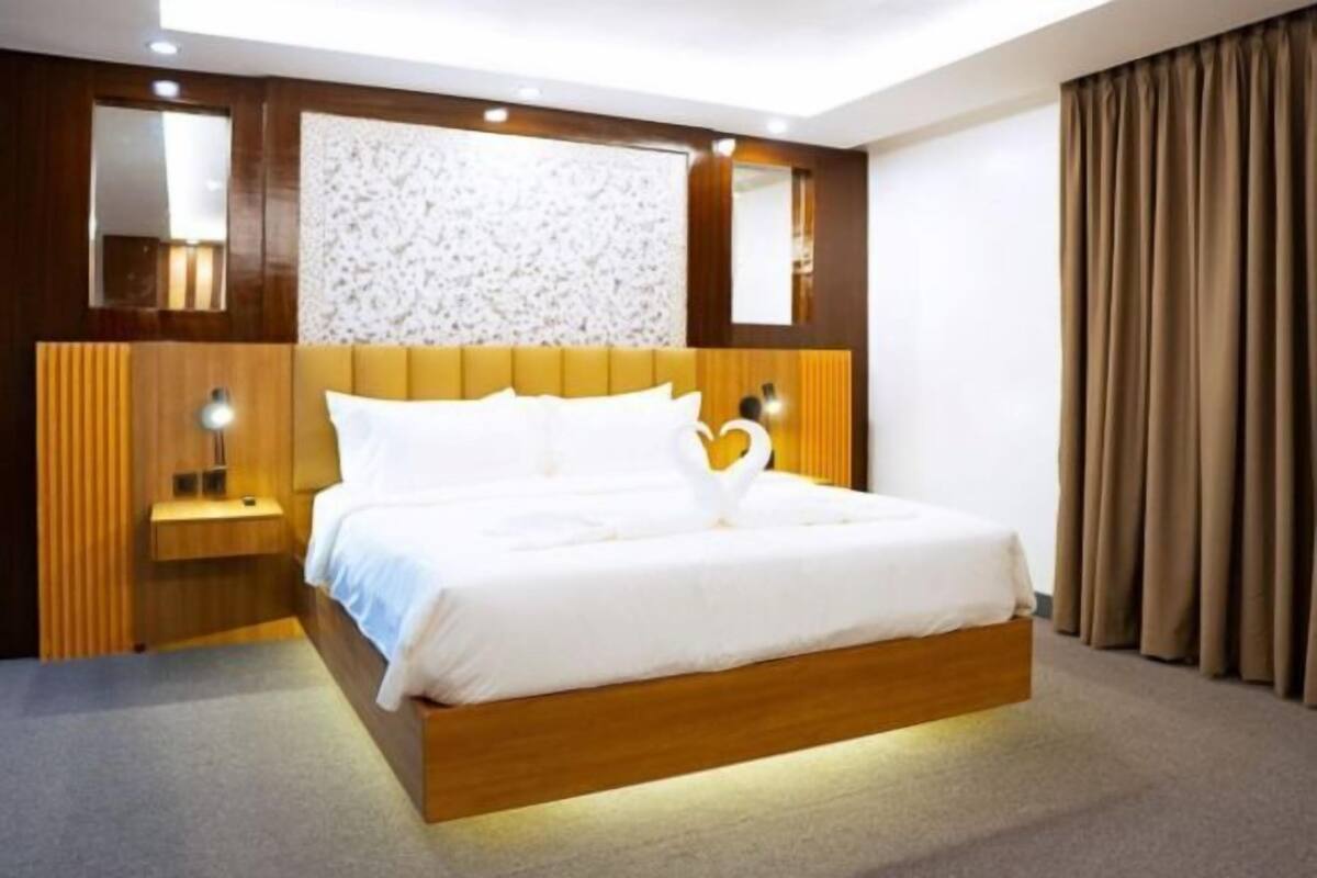 Une chambre d’hôtel moderne avec un cadre de lit en bois, une tête de lit ornée d’un panneau texturé, une table de chevet avec une lampe et un grand miroir.