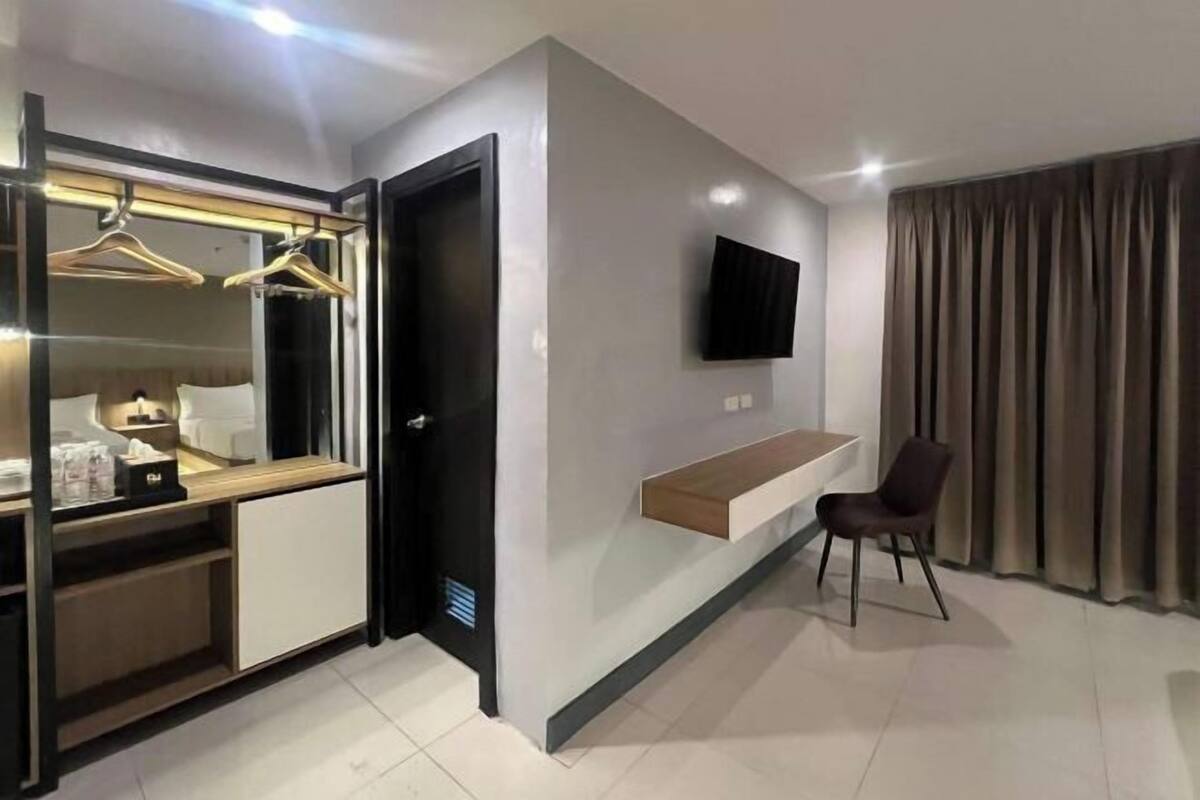 Une chambre d’hôtel moderne dotée d’un dressing, d’un téléviseur à écran plat fixé au mur, d’une console en bois et d’une seule chaise.