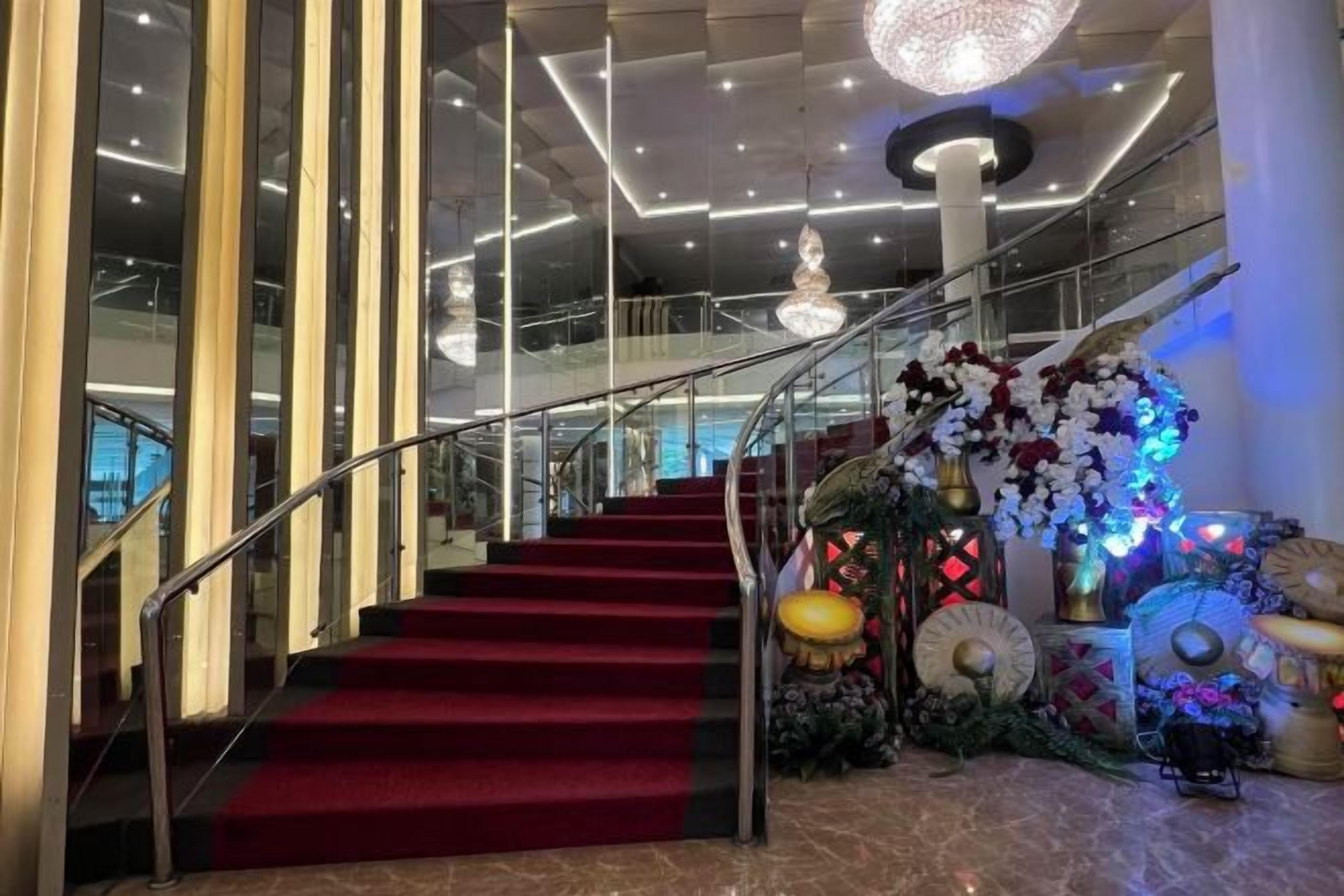 A grand staircase with a red carpet, leading to a balcony with a glass railing.