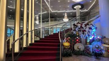A grand staircase with a red carpet, leading to a balcony with a glass railing.