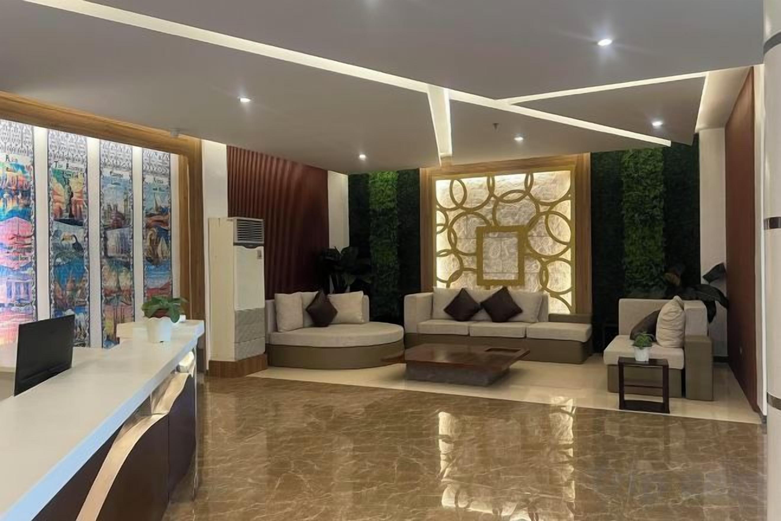 A modern hotel lobby with a reception desk, seating area, and decorative wall panels.