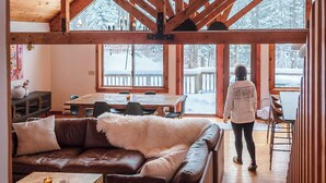 A spacious room with a high wooden ceiling, a large window, and a cozy seating area with a sofa and a table. - Designer 4-bedroom house in charming Stratton home sleeps 16 (Stratton)