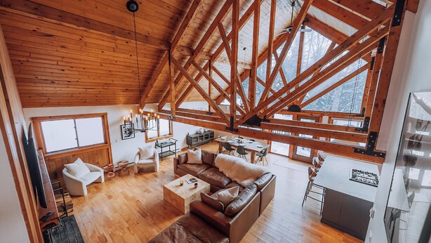 Ein geräumiges Loft mit hoher Decke und freiliegenden Holzbalken, ausgestattet mit einer gemütlichen Wohnbereitschaft inklusive Ledersofa, einem Esstisch und einer Küchenzeile.